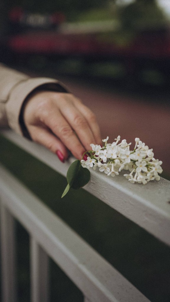 Крупный план руки на перилах рядом с веткой белой сирени. Ольга Грачёва