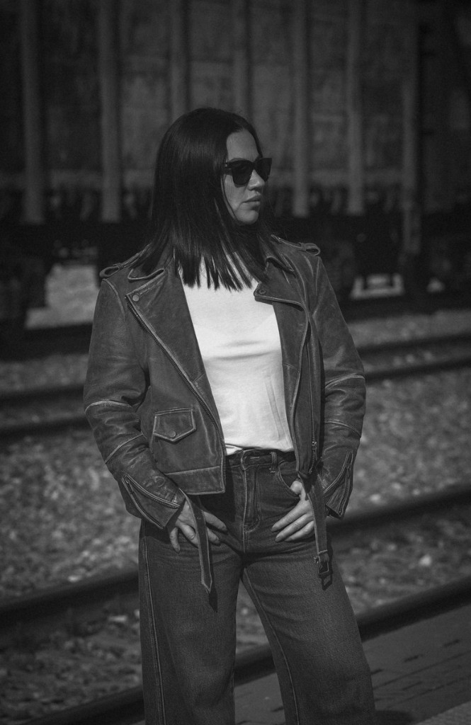 Чёрно-белый портрет у железнодорожных путей: кожаная куртка, очки, руки в карманах. Ольга Грачёва