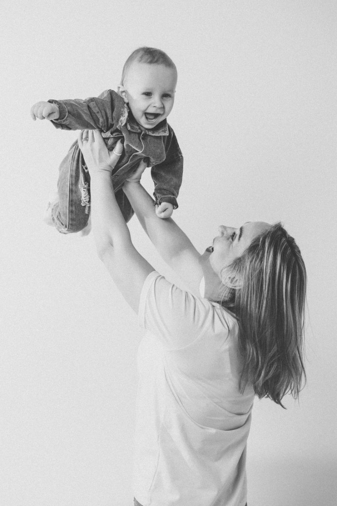 Чёрно-белый кадр: женщина поднимает ребёнка на руках, светлый фон. Ольга Грачёва